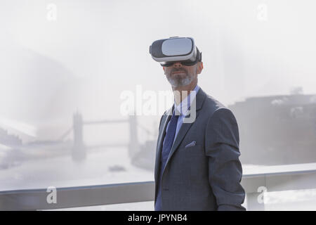 Businessman Using virtual reality simulator glasses on sunny urban pont sur la rivière Thames, London, UK Banque D'Images