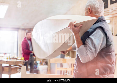 Les menuisiers d'hommes transportant du bois voile en atelier Banque D'Images