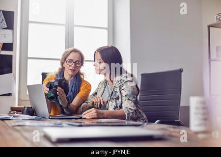 Femme avec appareil photo numérique photographes travaillant à laptop in office Banque D'Images