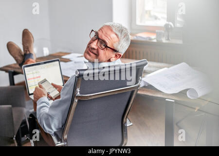 Portrait of smiling, confident businessman with cell phone and laptop in office