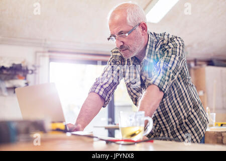 De graves senior male carpenter using laptop in workshop Banque D'Images