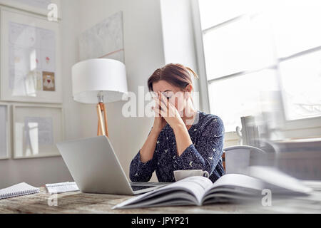 Fatiguée, stressée businesswoman at laptop with head in hands Banque D'Images