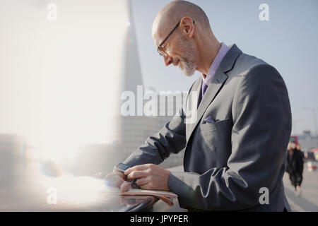 Businessman checking smart watch sur trottoir urbain ensoleillé, London, UK Banque D'Images
