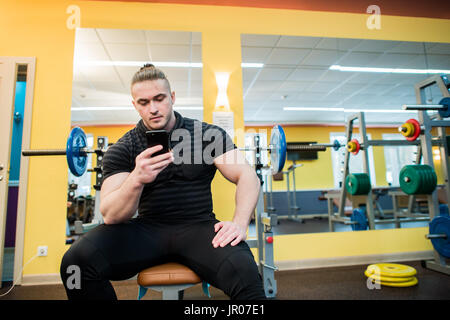 Jeune homme séduisant à l'aide de téléphone tout en ayant l'exercice en pause de sport. Banque D'Images