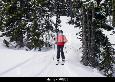 Une skieuse dans un manteau rouge le ski sur les pistes enneigées des montagnes Rocheuses ; Whistler, British Columbia, Canada Banque D'Images