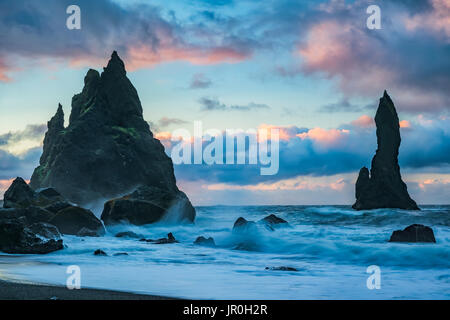 Les piles de la mer avec des vagues de Reynisdrangar connu sous le nom de Sunrise et passe au-dessus d'eux, Côte Sud ; l'Islande Banque D'Images