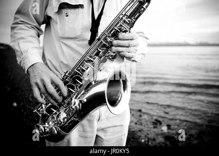 Un homme se jouant un saxophone sur la plage au bord de l'eau ; l'Alaska, États-Unis d'Amérique Banque D'Images