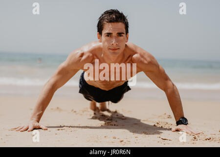 Homme remise en forme push-up faire l'exercice sur la plage. Portrait de monter son travail guy les muscles des bras et du corps avec des exercices de base pushup sur plage. Banque D'Images