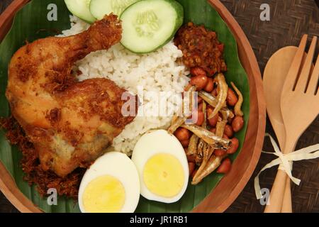 Nasi lemak, plat de riz savoureux malaisien avec du poulet frit, oeuf, arachide, d'anchois et de pâte de piment Banque D'Images