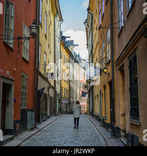 Une femme marchant dans une rue entre la vente au détail et les bâtiments résidentiels colorés ; Stockholm, Suède Banque D'Images