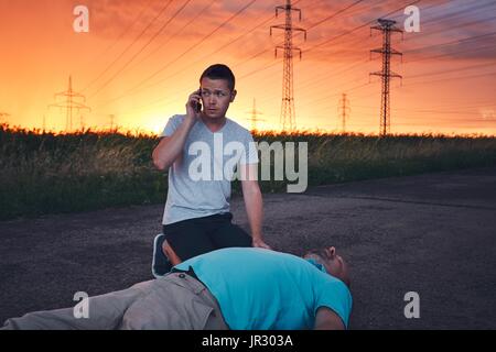 Jeune homme appelant à un service de secours. Réanimation spectaculaire sur la route au cours de tempête au coucher de soleil spectaculaire. Thèmes de sauvetage, aide et espoir. Banque D'Images