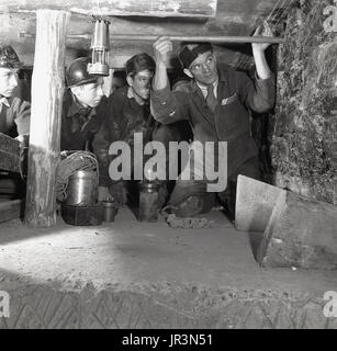 1948, historique, accroupi dans un puits de mine souterrain, un superviseur minier démontrant à certains stagiaires miniers une technique minière, en utilisant un poteau en bois pour vérifier le mur de la mine. Banque D'Images