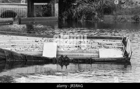 Petit bateau en bois abandonnés dans un lac et l'autre moitié sous l'eau. Noir et blanc. Banque D'Images