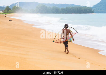 Pêcheur local Phuket accueil marche le long d'une plage de Phuket à partir de la pêche sur une journée tôt le matin en portant sa pêche primitive tools Banque D'Images