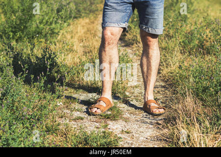 Dans les jambes des hommes sandales en cuir marron et bleu jean short debout sur un sentier Banque D'Images