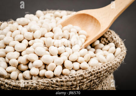 Haricots blancs en sac sac avec du scoop sur fond noir. Banque D'Images