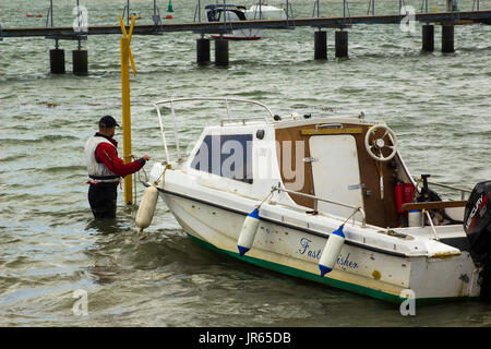 Un propriétaire de bateau, portant son petit bateau en fibre de verre vers la rive à Warsash, Hampshire pour une remorque en attente de prendre hors de l'eau Banque D'Images