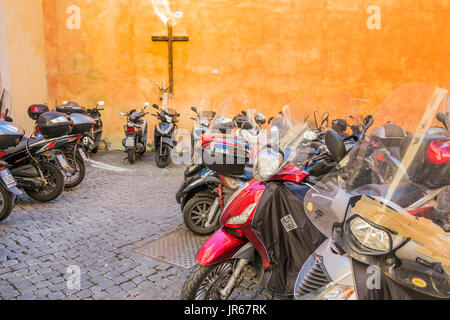 Scooters romain, garée dans une cour avec une croix sur le mur arrière, Rome, Latium, Italie Banque D'Images