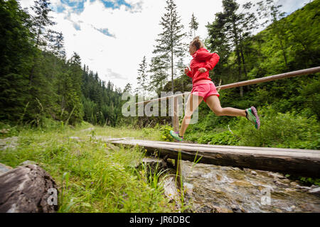 Jeune femme tournant dans les montagnes de l'été journée ensoleillée. Femme Trail Runner crossing bridge sur une rivière de montagne. Concept Sport et fitness en plein air dans n Banque D'Images