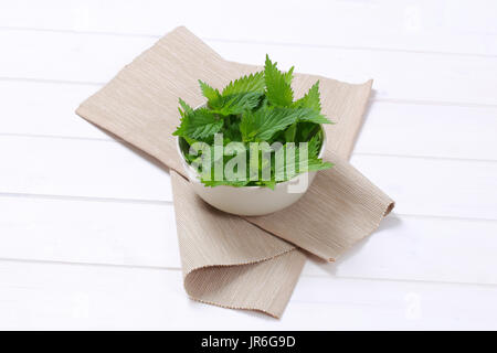 Bol de feuilles d'orties fraîches sur place beige mat Banque D'Images