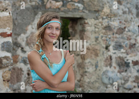 Young blonde woman wearing turquoise haut standing contre mur en pierre médiévale et souriant Banque D'Images