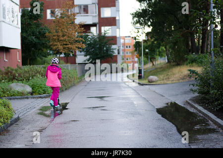 Stockholm, Suède. 4e août, 2017. Jour de pluie à Stockholm après plusieurs jours avec des chaudes journées d'été sans pluie. Fille en vêtements de pluie colorées et des bottes en caoutchouc rides son kick-bike dans les rues des pluies. Credit : Jari Juntunen/Alamy Live News Banque D'Images