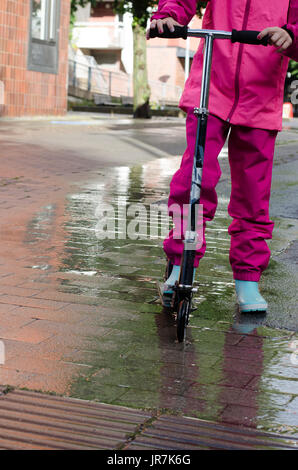 Stockholm, Suède. 4e août, 2017. Jour de pluie à Stockholm après plusieurs jours avec des chaudes journées d'été sans pluie. Fille en vêtements de pluie colorées et des bottes en caoutchouc rides son kick-bike dans les rues des pluies. Credit : Jari Juntunen/Alamy Live News Banque D'Images