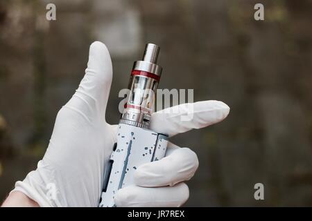 Main dans white glove holding cigarette électronique avec des bandes rouges sur fond sombre. Banque D'Images