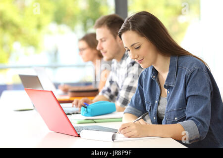 La rédaction de notes d'étudiants dans une classe avec d'autres camarades dans l'arrière-plan Banque D'Images