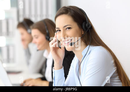 Télévendeur heureux vous regarde au bureau avec les autres travailleurs dans l'arrière-plan Banque D'Images