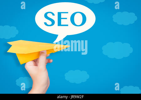 Hand holding paper plane avec seo en bulle sur fond bleu Banque D'Images