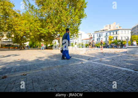 Un prêtre grec orthodoxe porte une serviette pendant qu'il marche à travers Athènes tandis qu'un groupe de coureurs s'exécute par lui et avis Banque D'Images