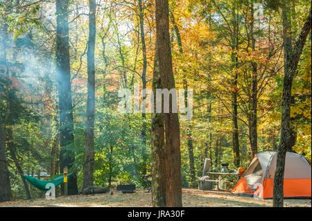 Tente camping-se reposant dans un hamac comme la fumée de feu de camp au milieu des arbres les prises du soleil sur un beau matin d'automne dans les montagnes Blue Ridge. (USA) Banque D'Images