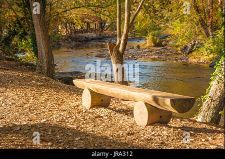 Sunlit split-log banc le long de la paisible rivière Chattahoochee sur un magnifique coucher de soleil en automne à Helen, la Géorgie. (USA) Banque D'Images