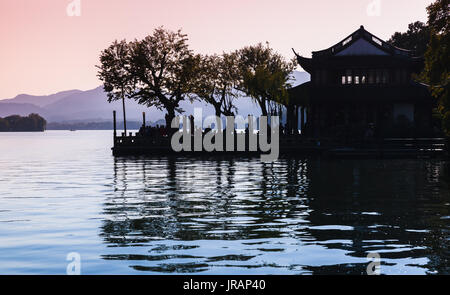 La silhouette des arbres noirs et chinois traditionnel des bâtiments sur la côte du lac de l'Ouest. Célèbre parc public de la ville de Hangzhou, Chine Banque D'Images