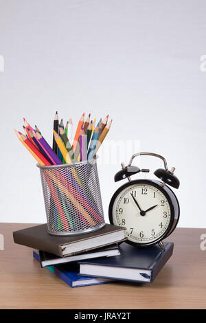Une pile de livres scolaires et de journal à l'aide de crayons et réveil sur un bureau en bois d'un retour à l'école, l'apprentissage thème. Banque D'Images