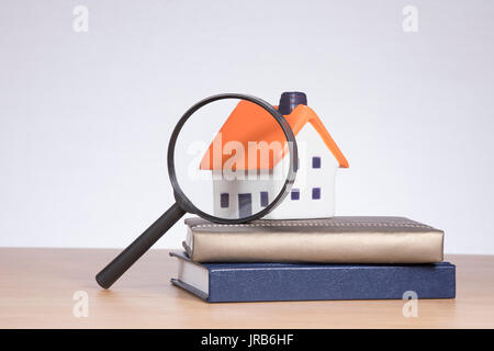 Un modèle de maison sur une pile de livres de banque sous une loupe avec copie blanche espace dans un marché immobilier à thème de recherche concept. Banque D'Images