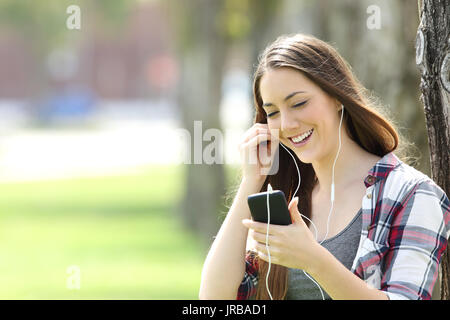 Happy girl à l'écoute sur la musique en ligne et de regarder du contenu multimédia dans un téléphone intelligent dans un parc Banque D'Images