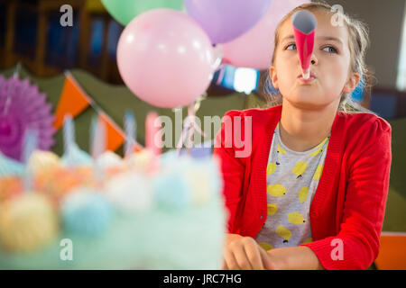 Cute girl blowing party horn lors d'anniversaire à la maison Banque D'Images