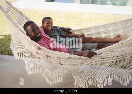 Portrait of smiling père et fils de vous détendre sur un hamac dans le jardin Banque D'Images