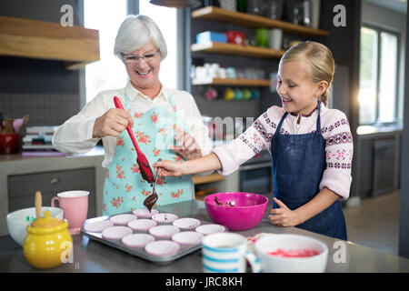 Aider grand-mère souriante petite-fille en versant la pâte dans le plateau cupcake Banque D'Images