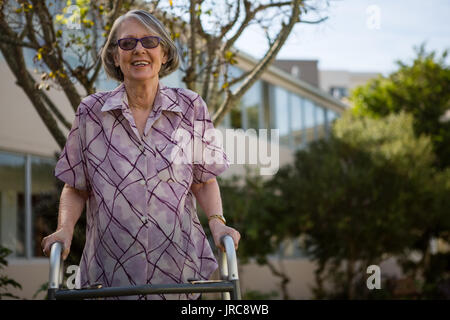 Portrait of senior woman holding walker tout en se tenant debout dans une cour Banque D'Images