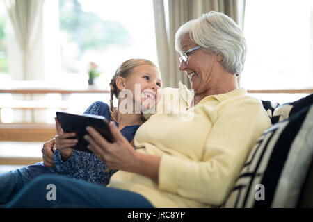 Petite-fille et grand-mère Smiling sitting on sofa in living room Banque D'Images