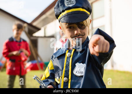 Portrait de jeune garçon en costume de police faisant des gestes tout en se tenant debout dans une cour Banque D'Images