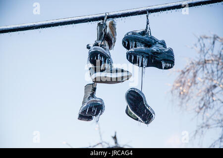 Chaussures attachées ensemble par leurs lacets sont suspendues à une ligne. Mais après une tempête de glace, ils sont recouverts d'une épaisse couche de glace, formant de nombreux glaçons Banque D'Images