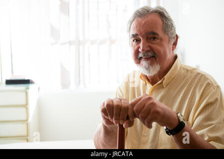 Portrait of happy senior man holding canne en position assise, dans une maison de soins infirmiers Banque D'Images