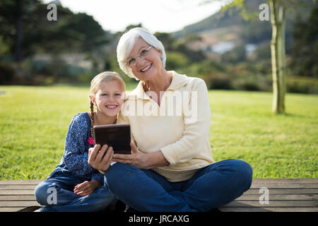 Petite-fille et grand-mère souriant assis sur le pont with digital tablet Banque D'Images