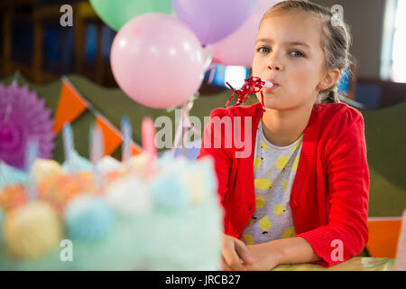 Cute girl blowing party horn lors d'anniversaire à la maison Banque D'Images