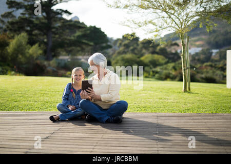 Petite-fille et grand-mère souriant assis sur le pont with digital tablet Banque D'Images