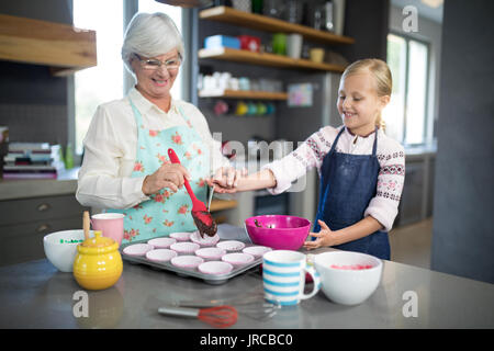 Aider grand-mère souriante petite-fille en versant la pâte dans le plateau cupcake Banque D'Images